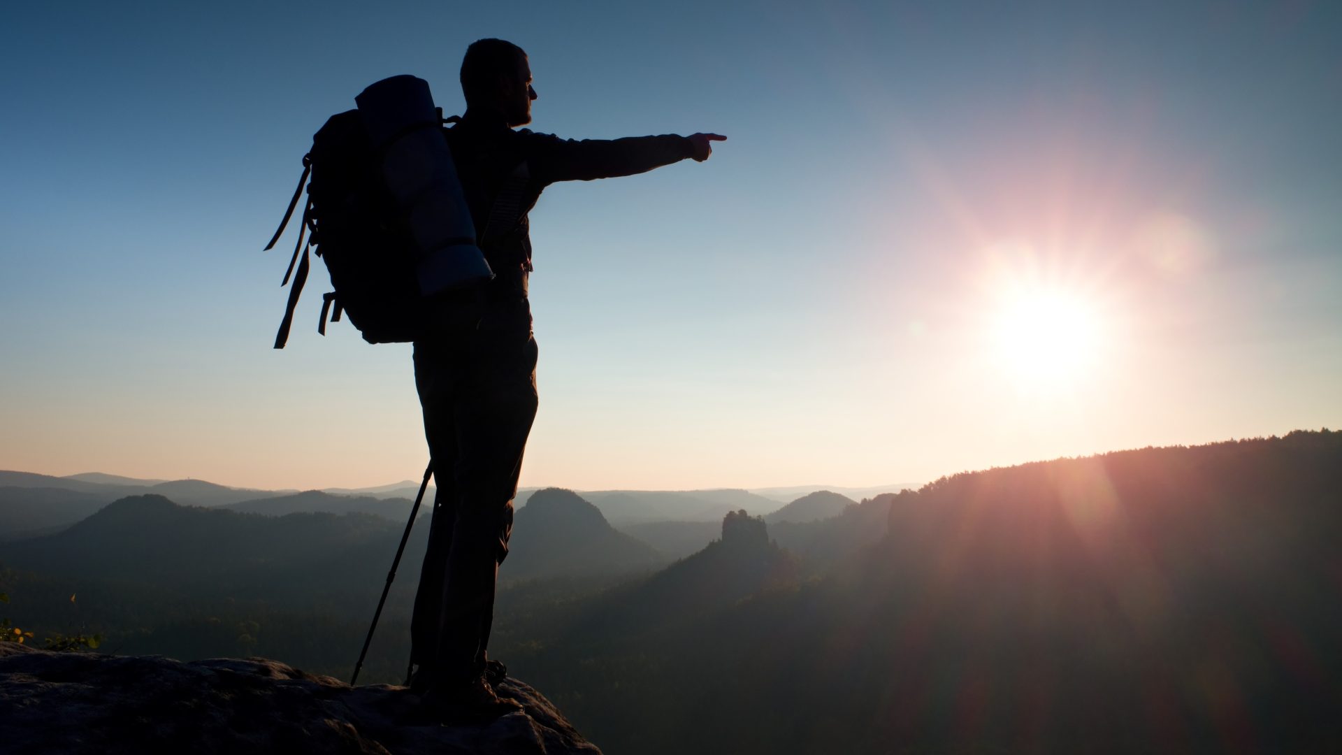 The silhouette of a man on top of a mountain points to the right.