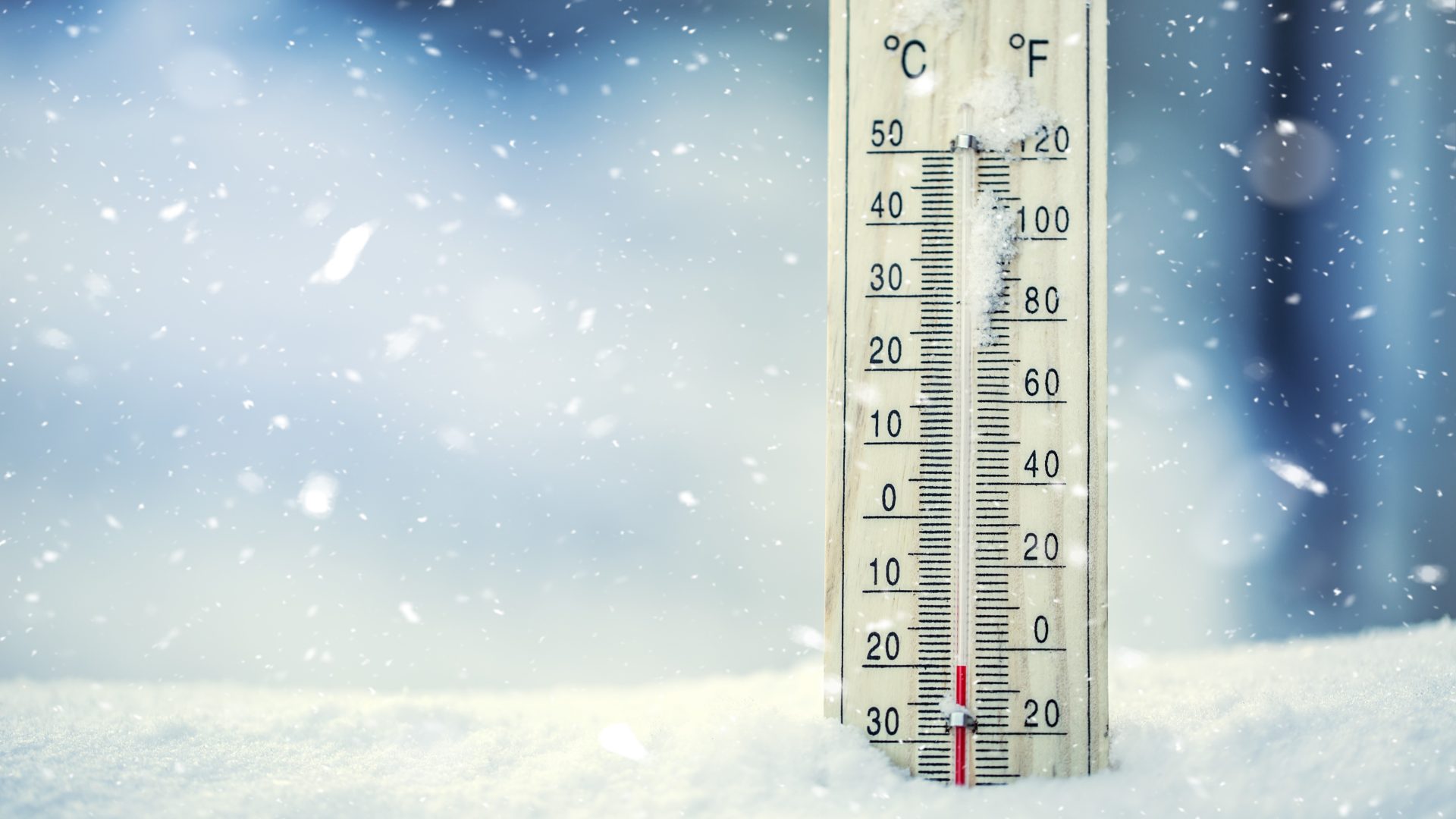 A thermometer on snow shows a low temperature in Celsius and Fahrenheit.