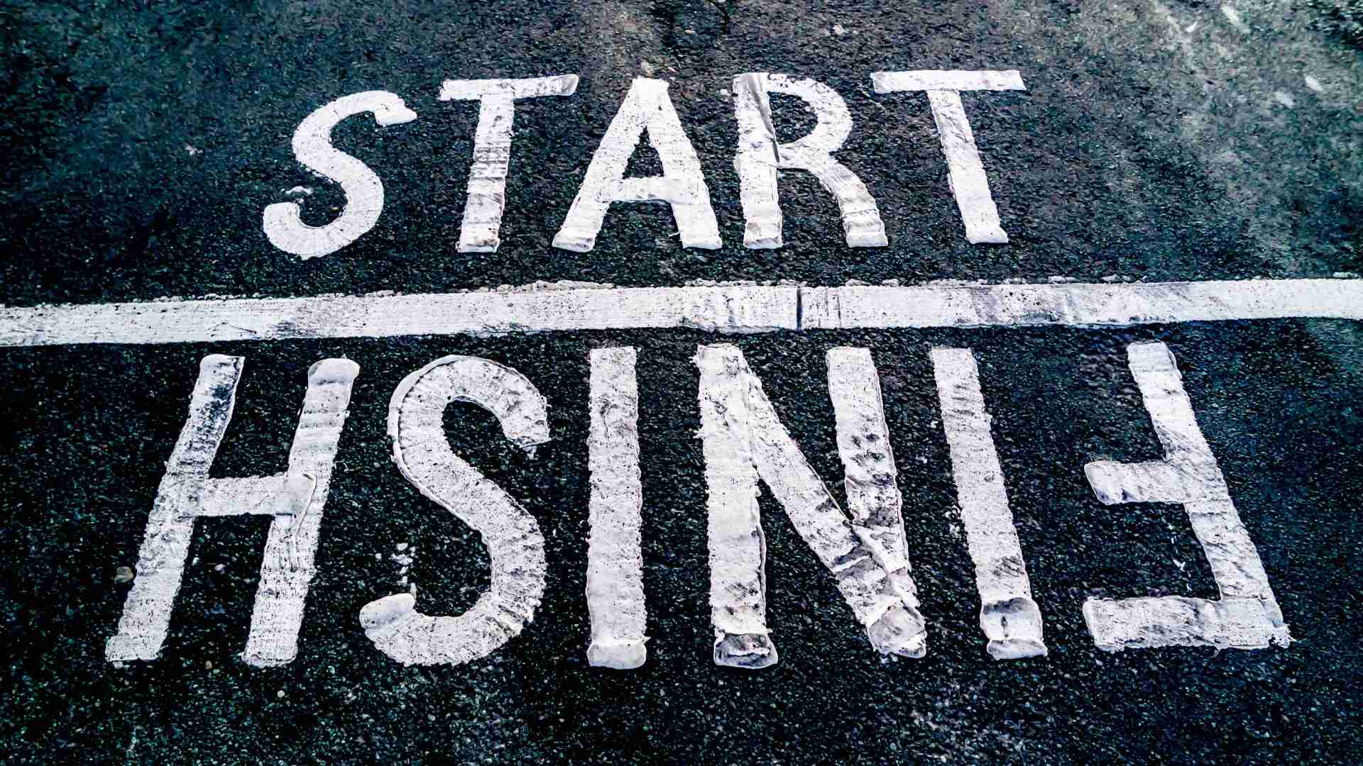 The image is of an asphalt street with a start and finish line. The word “start” is above a white line, and the word “finish” is upside down below the line.