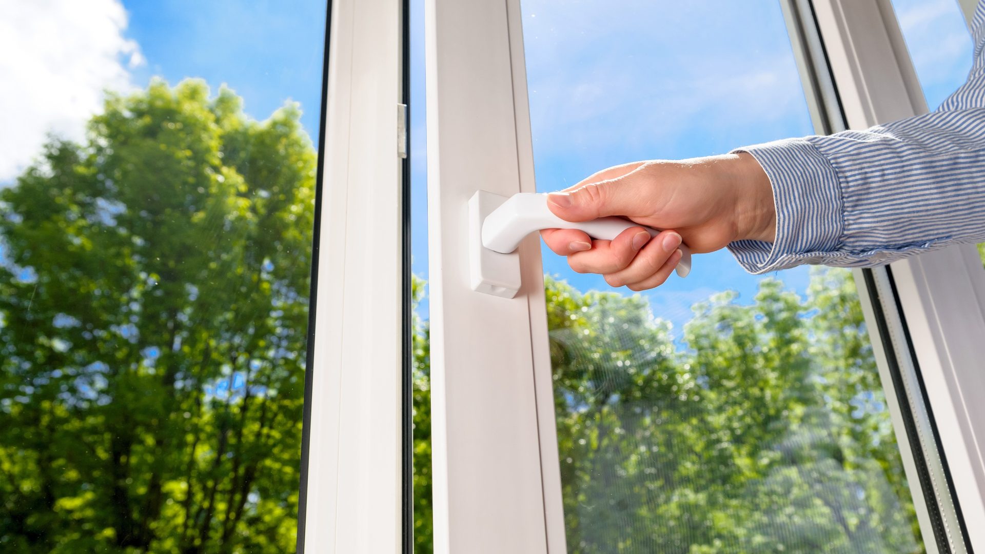 Close view of a hand opening a large vinyl window against a sunlit background