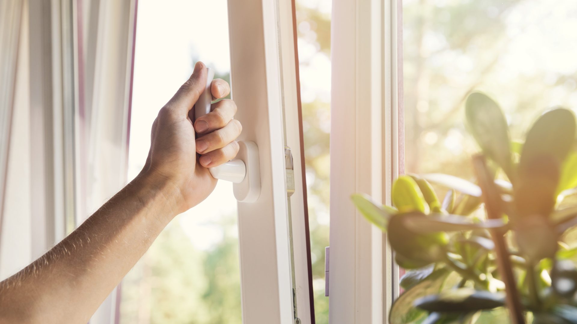 Close view of a hand opening a beautiful vinyl window against a sunlit exterior backdrop