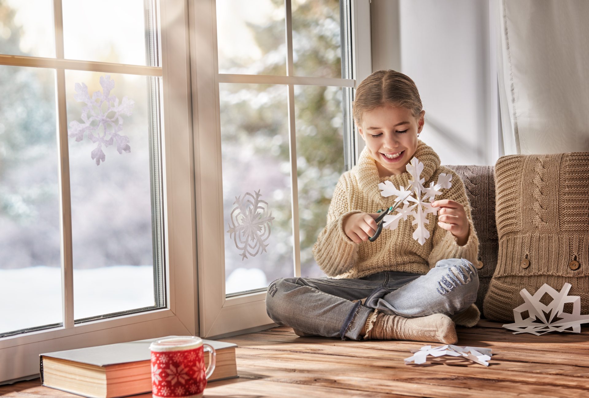 A child cuts out paper snowflakes while sitting in front of a new virgin vinyl replacement window