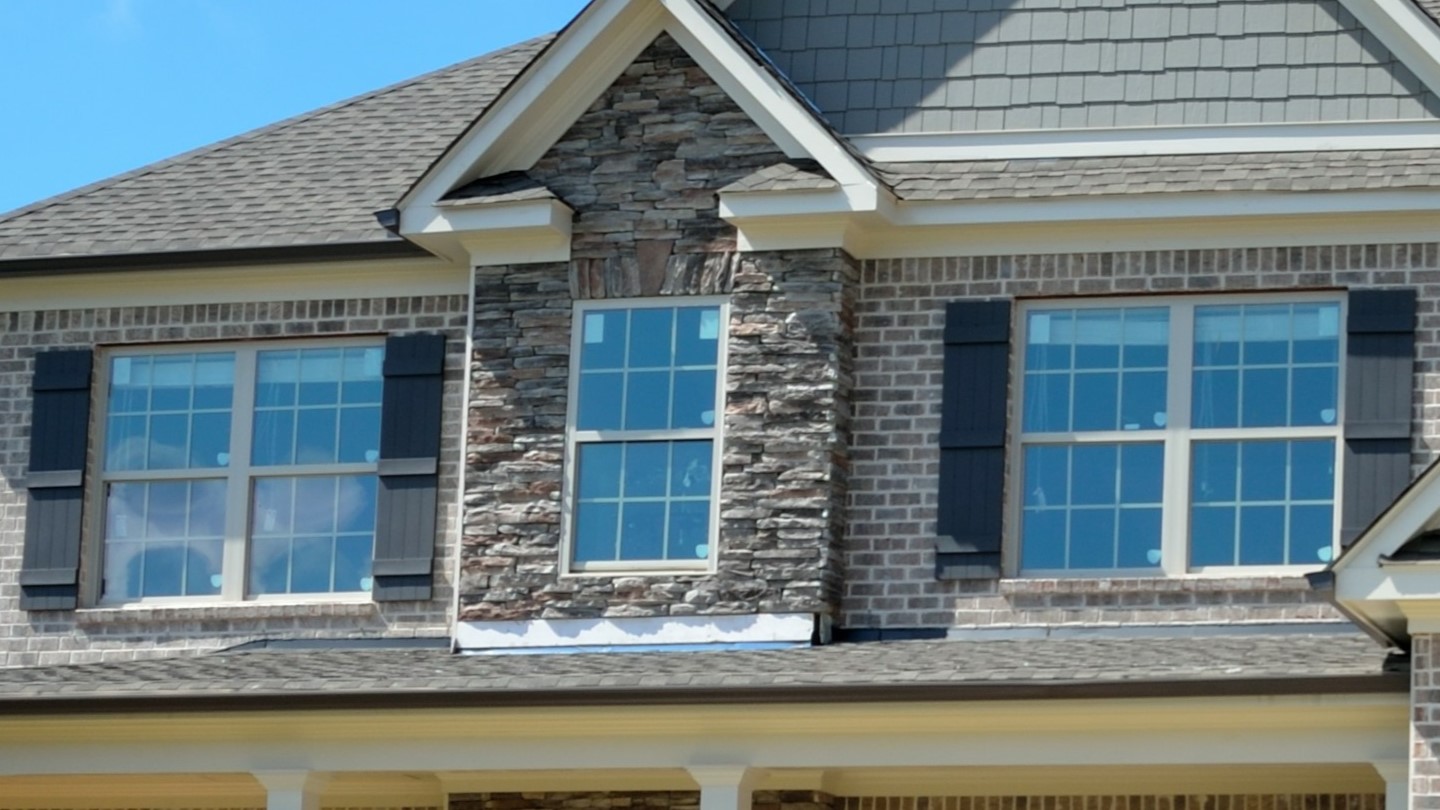 Exterior view of large home with dark brick siding and newly installed windows on second floor