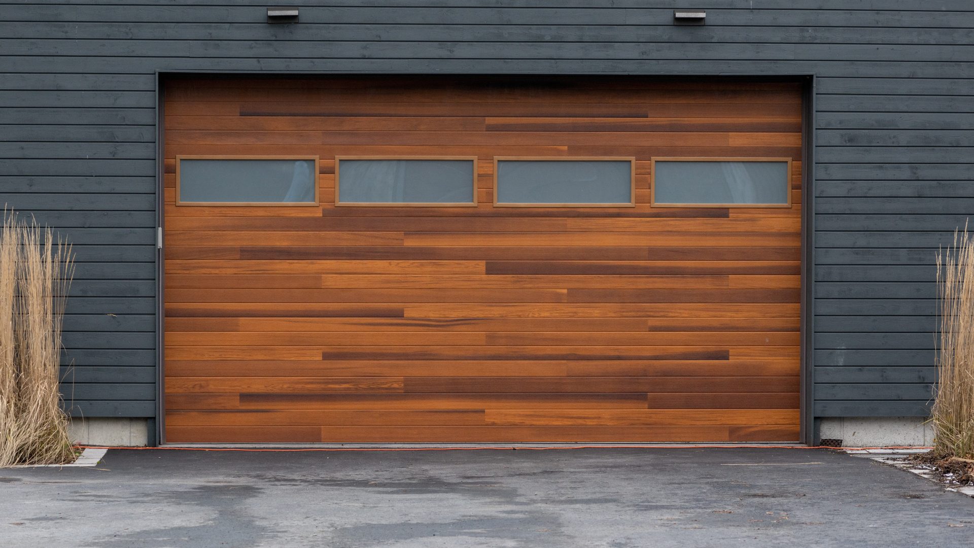 Frontal view of a beautiful wooden garage door with narrow windows installed on a grey house