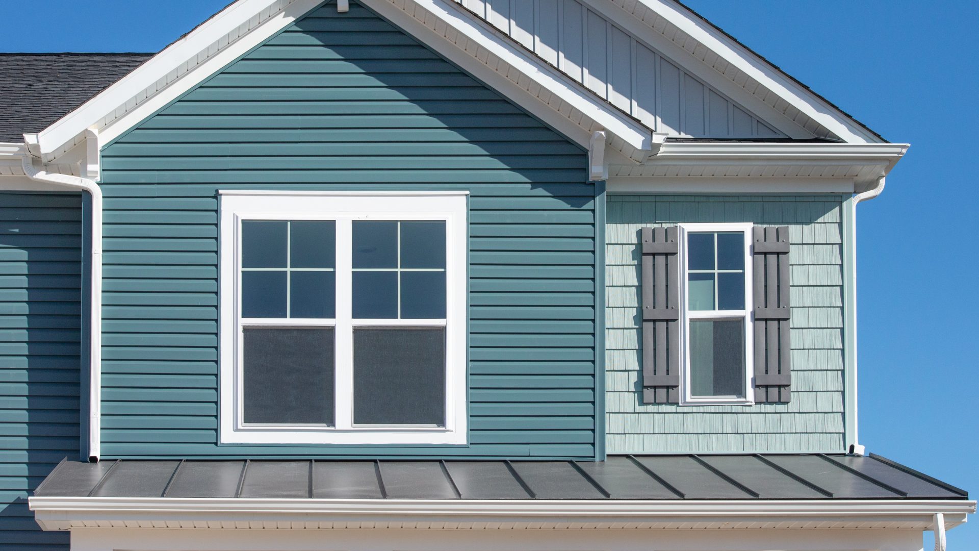 Close-up of home roof gable with blue siding and two new vinyl windows