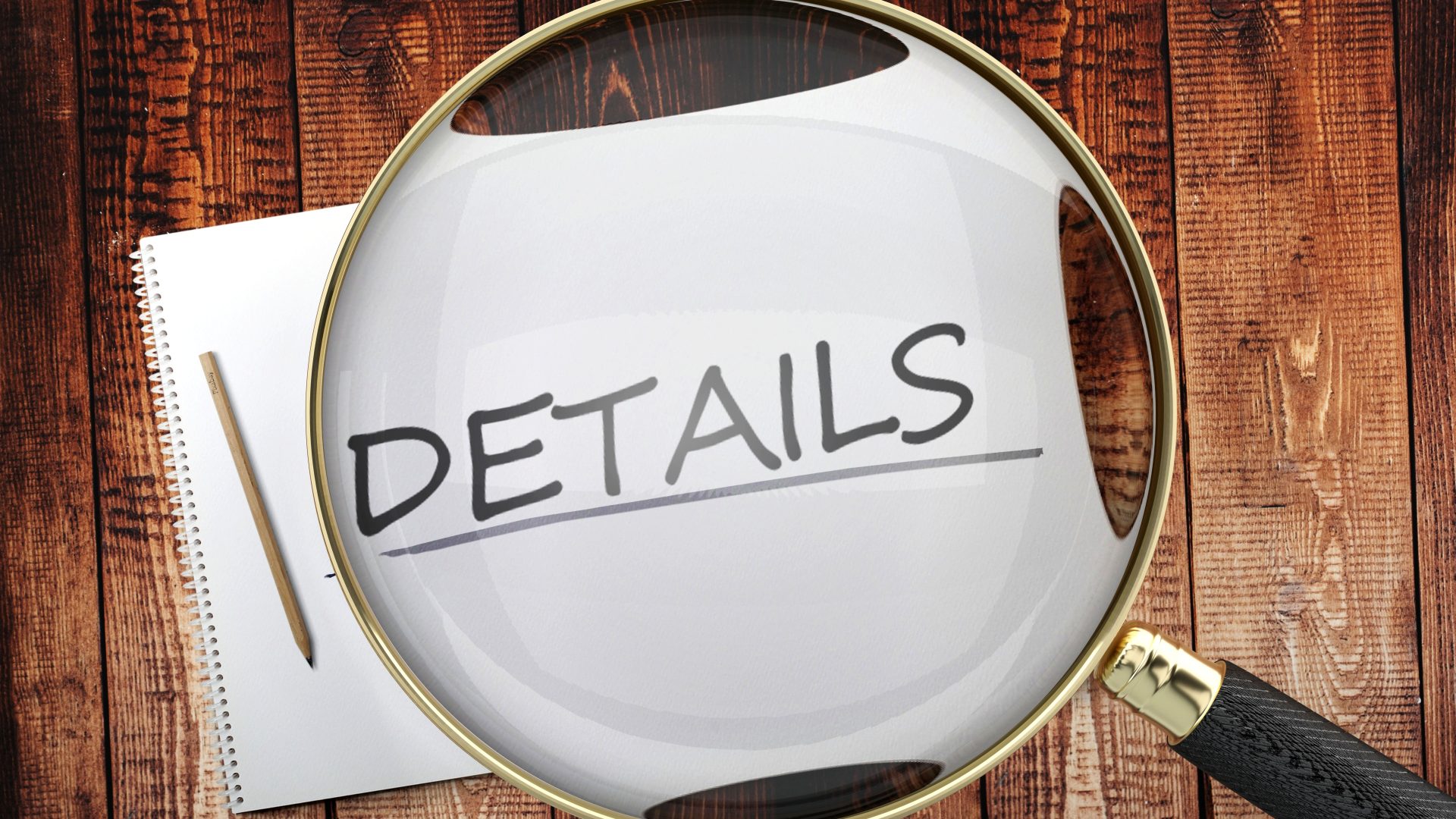 Close view of a magnifying glass hovering over and enlarging a piece of paper reading “Details” that sits on top of a table or desk