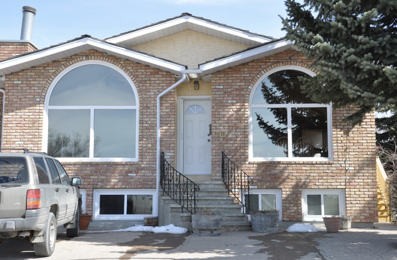 A brick home featuring two large arched windows with white frames on either side of a centered white front door and stairway with black railings