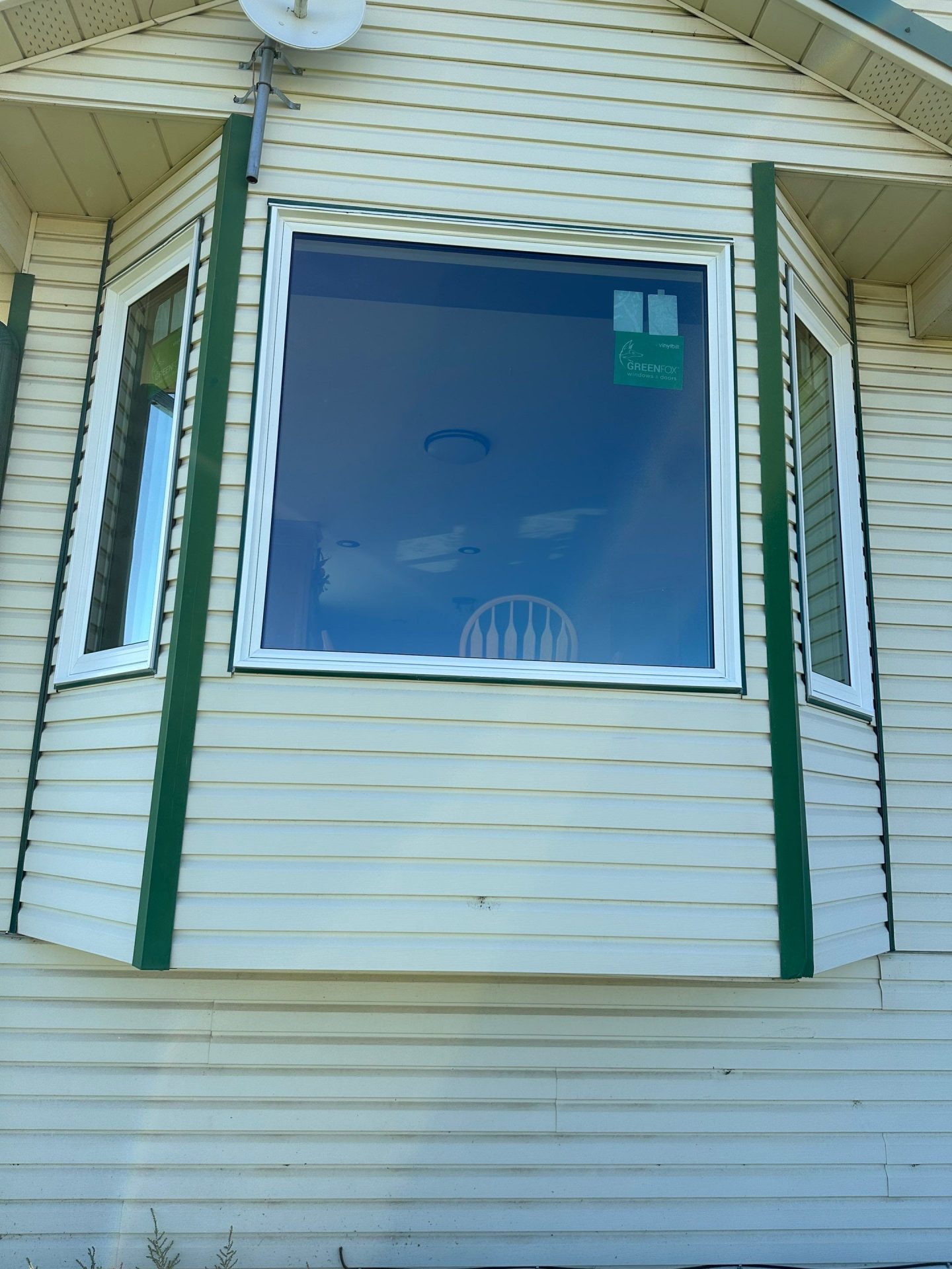 A large bay window with a white vinyl frame and clear glass installed on the exterior of a beige vinyl-sided home