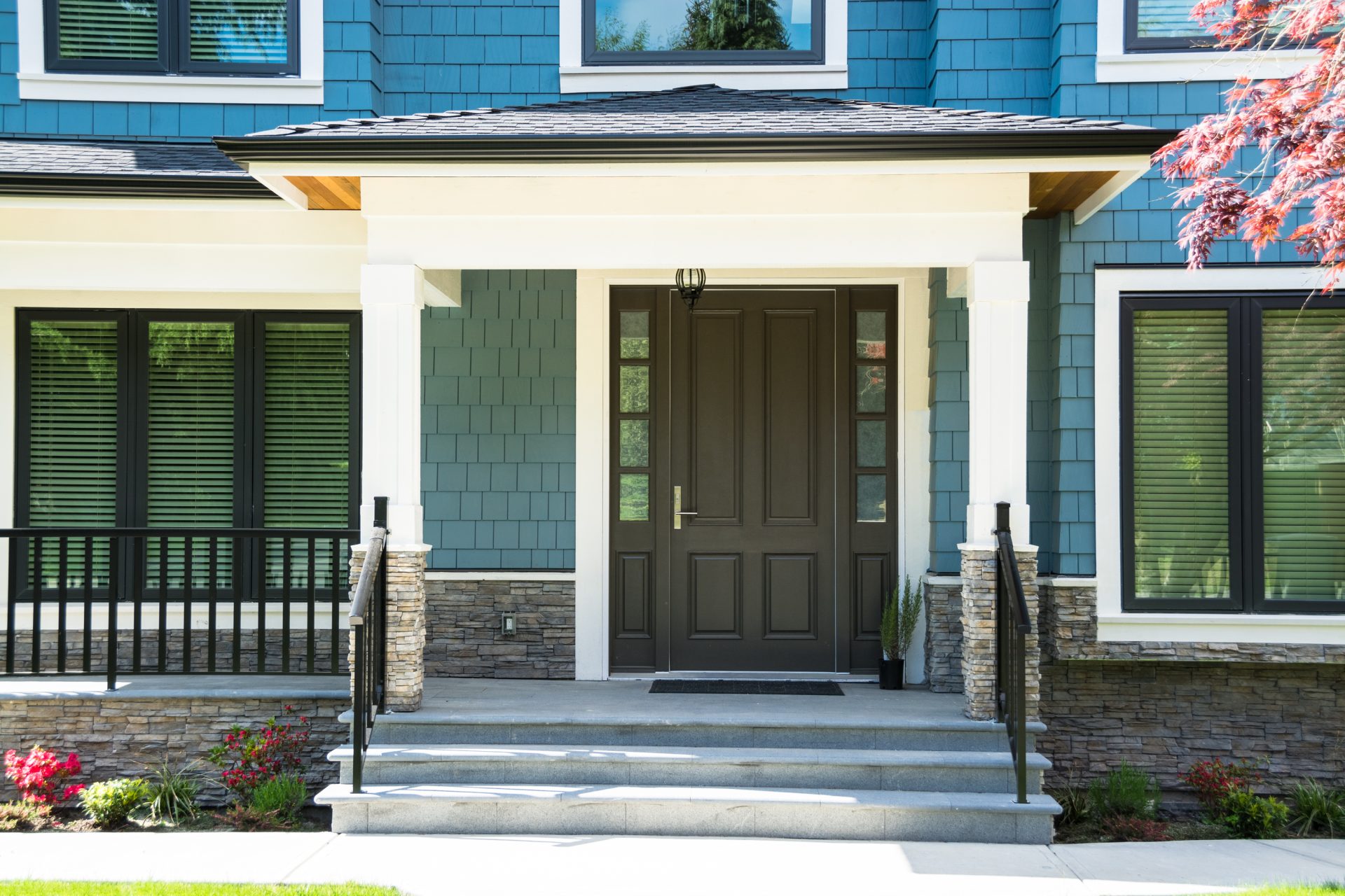 A brown door on a blue house with a stone base and cement steps