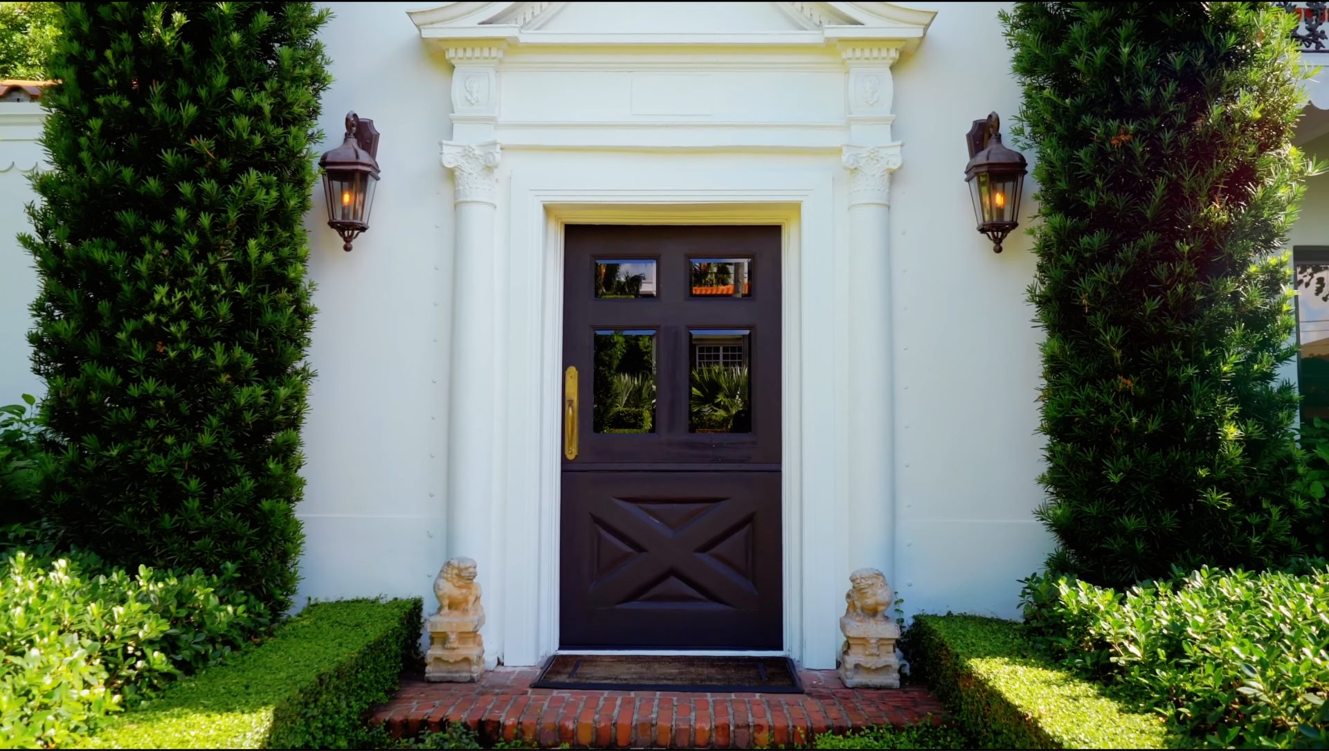 A black front door with a gold handle on a white house with a brick step.