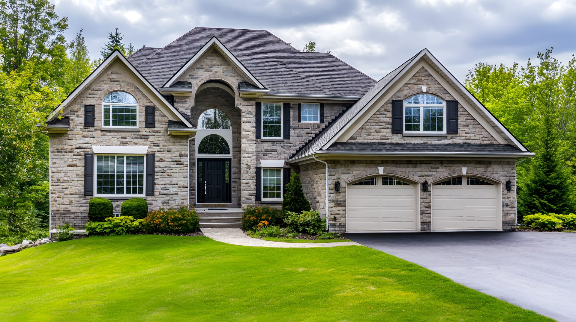 A large gray two-story home with a stone base, many windows, and a wood door with glass inserts.