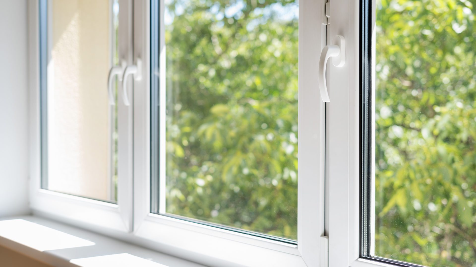 Close, angled view of a bank of vinyl windows with sunlit trees in the background