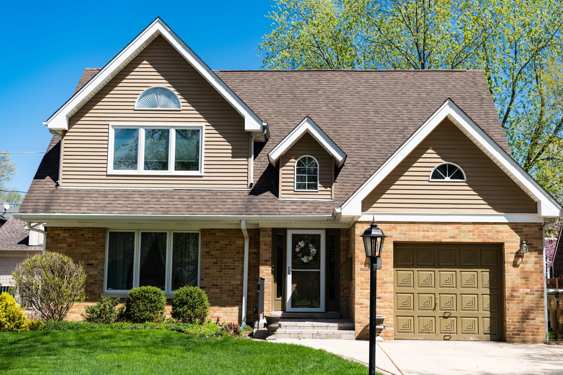 A tan and brick house with an asphalt shingle roof, several windows, and a wood door with a storm door in front.