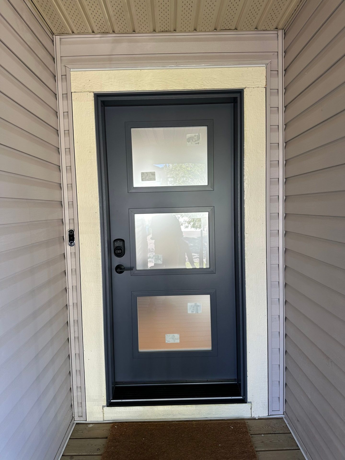 A blue front door with a black handle, black code box, and three glass inserts on a white house