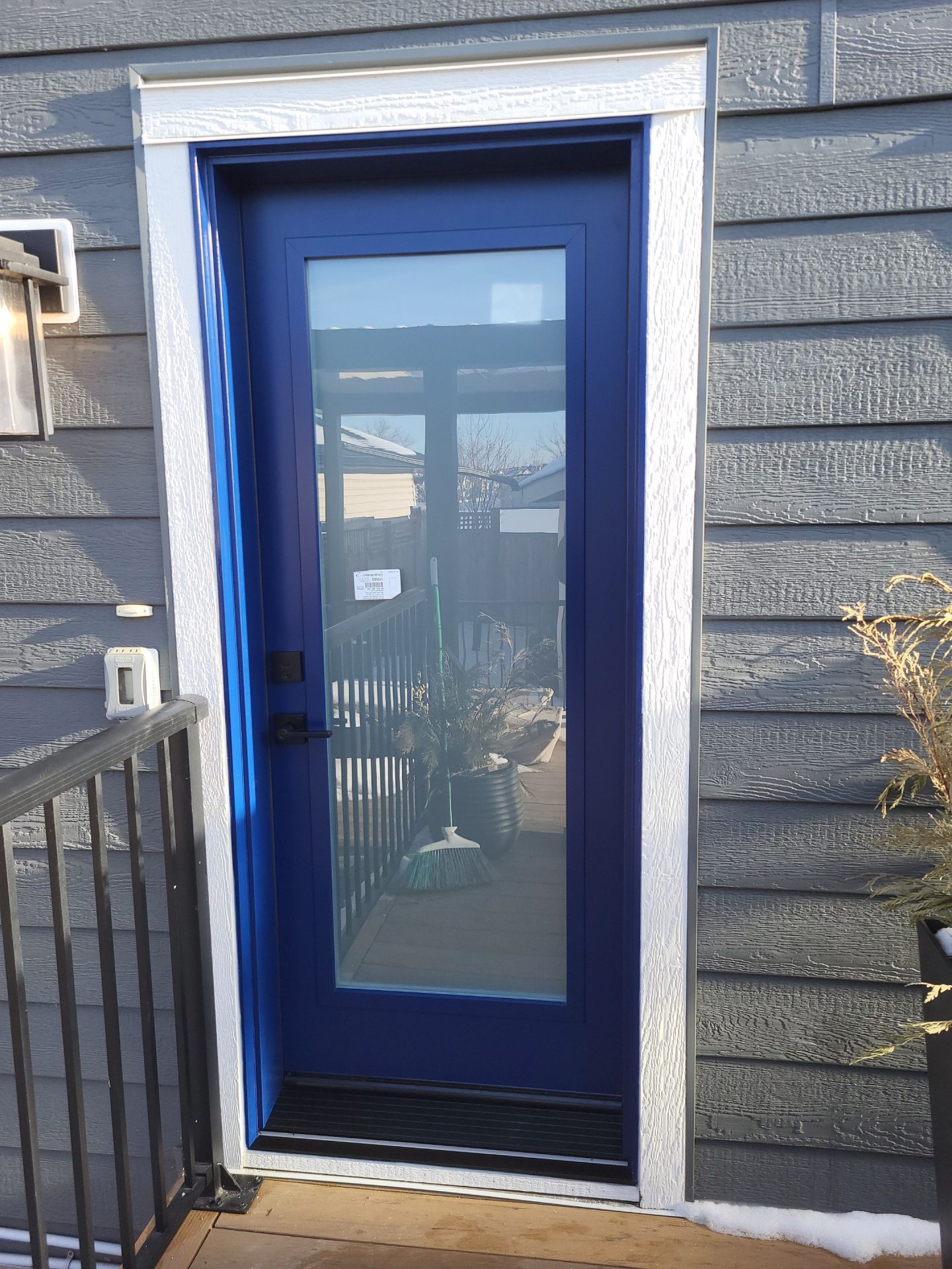 A blue door with a large glass insert and a white frame on a gray house