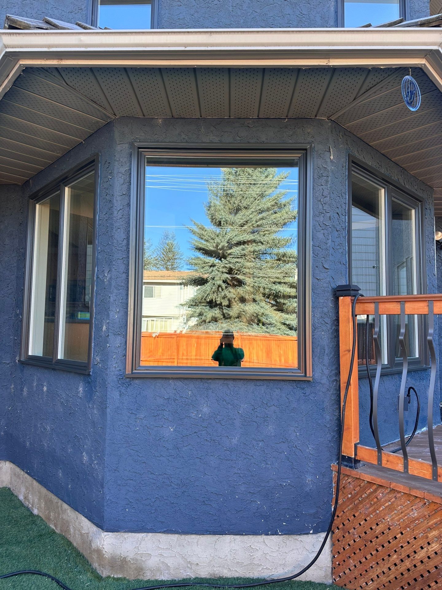 A picture window on a blue house with an overhang.