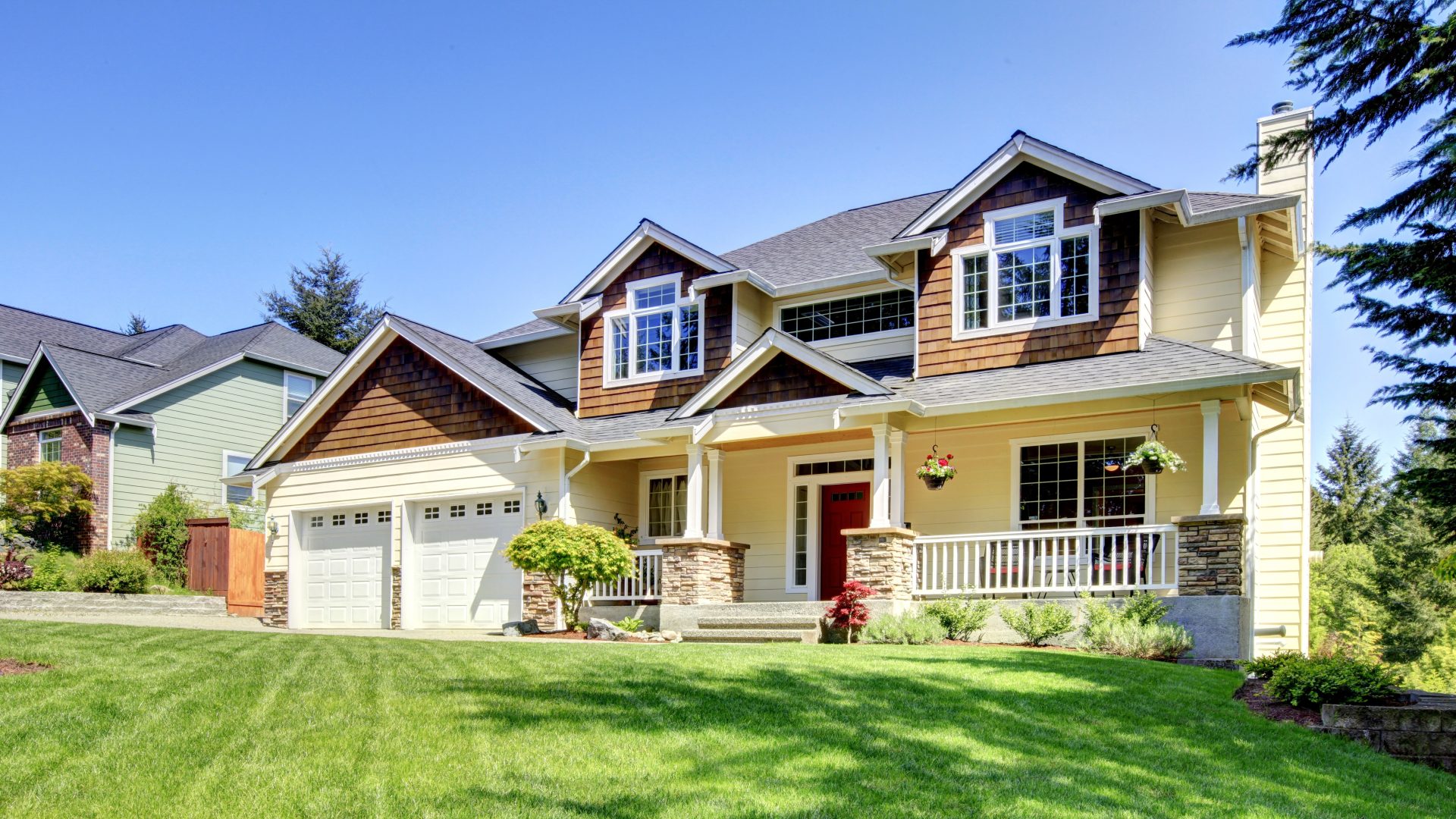 Large two-story home with mixed siding textures, white trim, and a covered front porch overlooking a landscaped lawn.