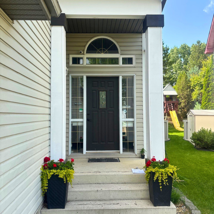 Black front door with arched transom, tall sidelights, white columns, beige siding, concrete steps, planters, and green lawn